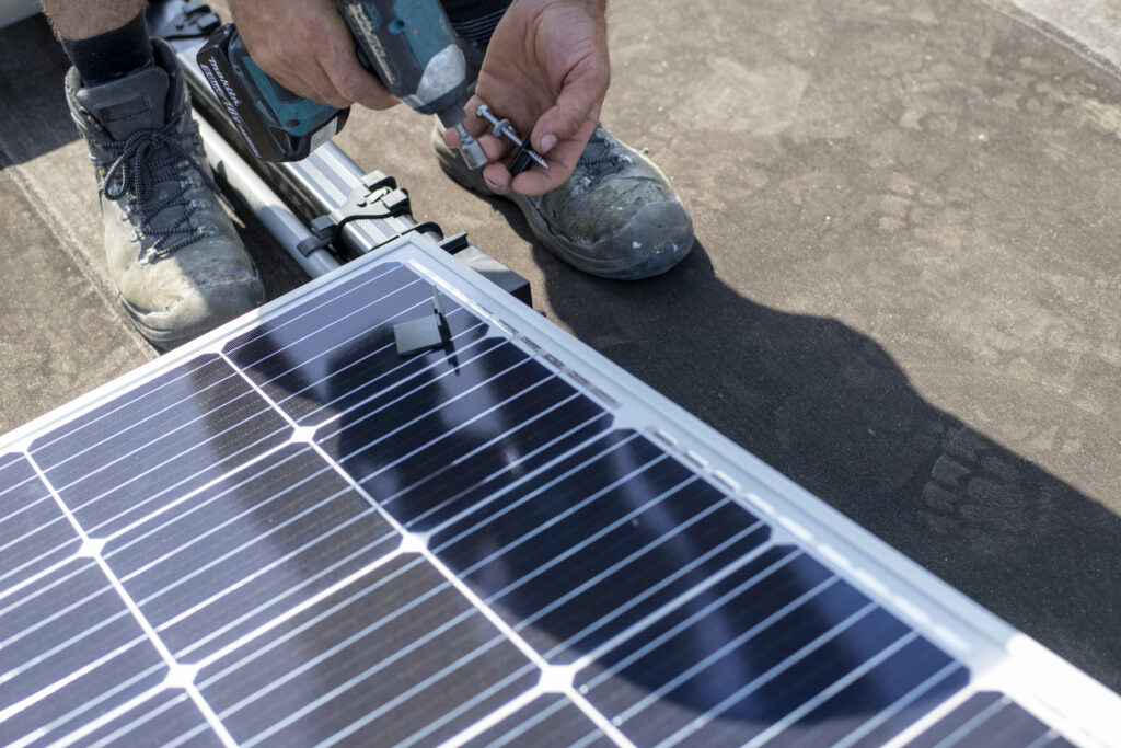 A worker installs a solar panel on a sunny day.